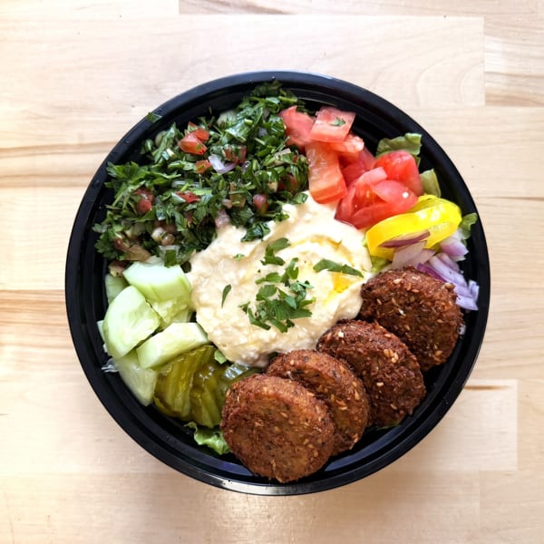 Falafel bowl with hummus, tabbouleh, diced tomatoes, cucumbers, pickles, and peppers.