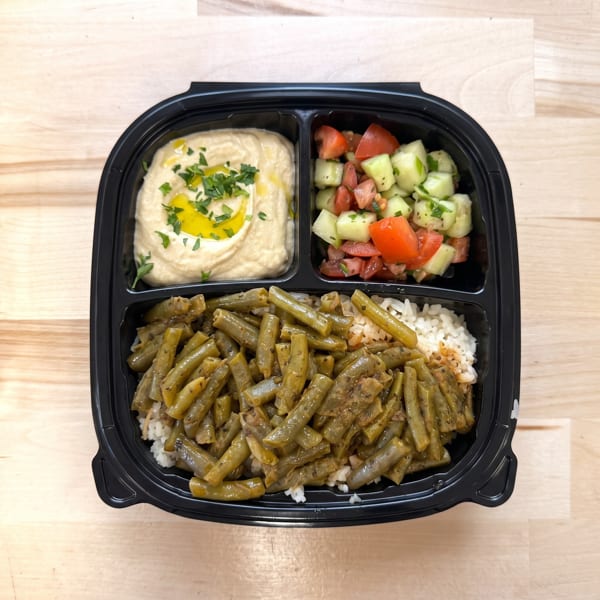 Black to-go container with hummus, cucumber tomato salad, and green beans over rice.